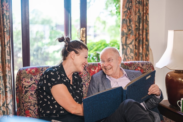 older man and family member on a sofa laughing together with a book