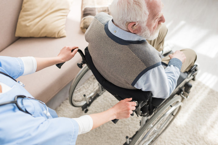 High angle view of nurse standing behind disabled grey haired man in wheelchair
