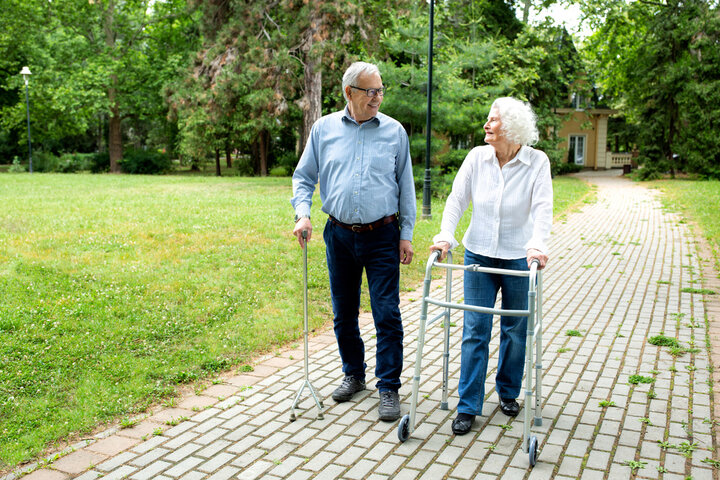 Senior man using a walking cane accompanied by a senior lady strolling with folding walker